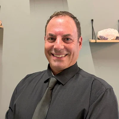 Dr. David Liberman smiling at the camera while wearing a black shirt and tie